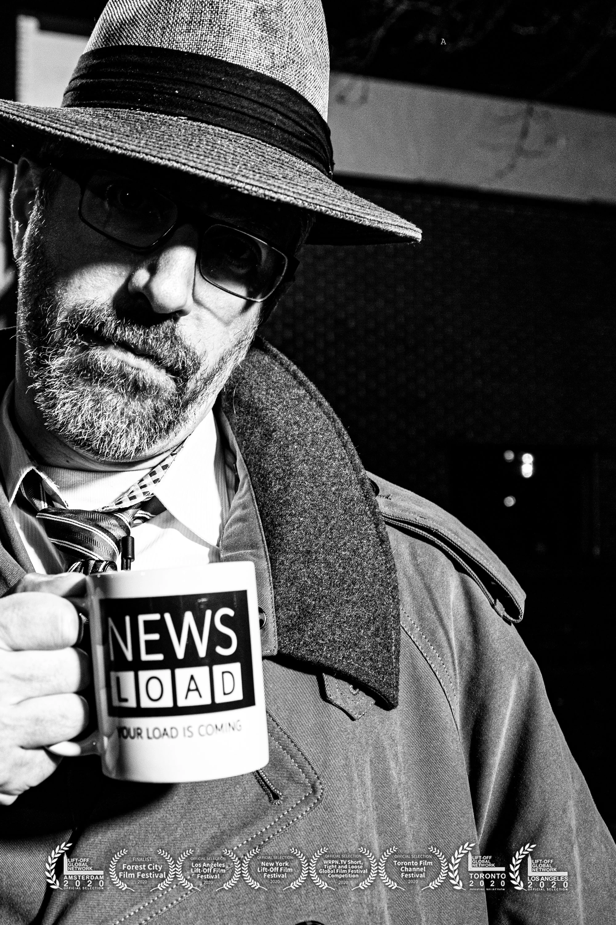 A man wearing a fedora, glasses, and a trench coat holds a white mug with "NEWS LOAD" and "YOUR LOAD IS COMING" printed on it, against a dark background with faint lights.