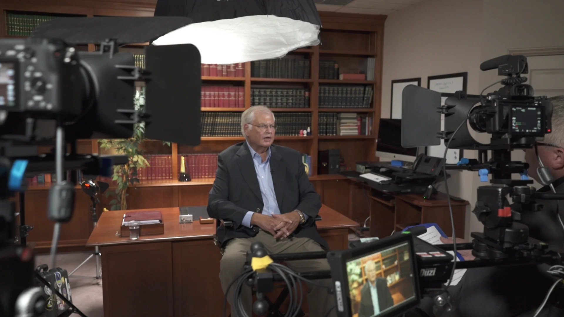 The setup. A man being interviewed at a desk, cameras and lights aimed at him — the room as it actually was.