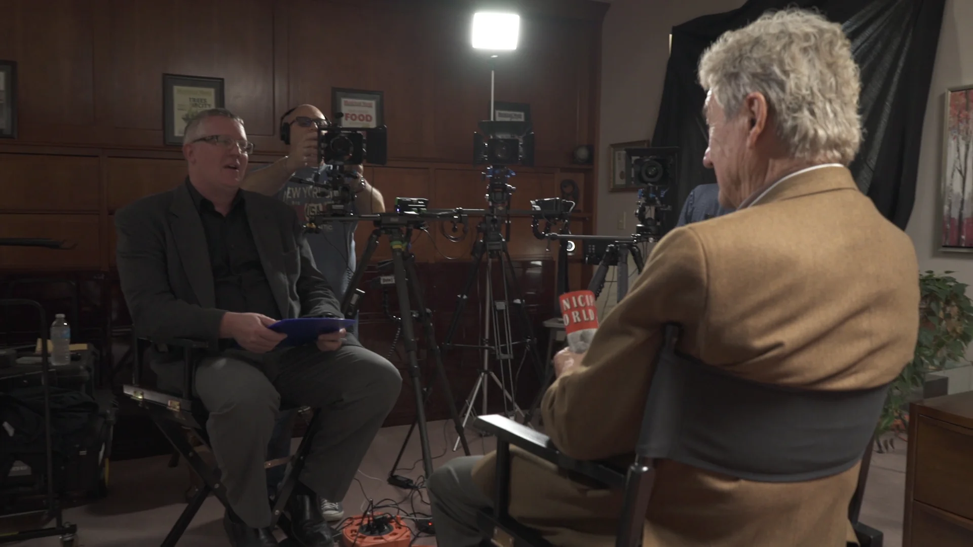 The crew at work. Two people seated, gear in the background, camera operator's shirt in frame.