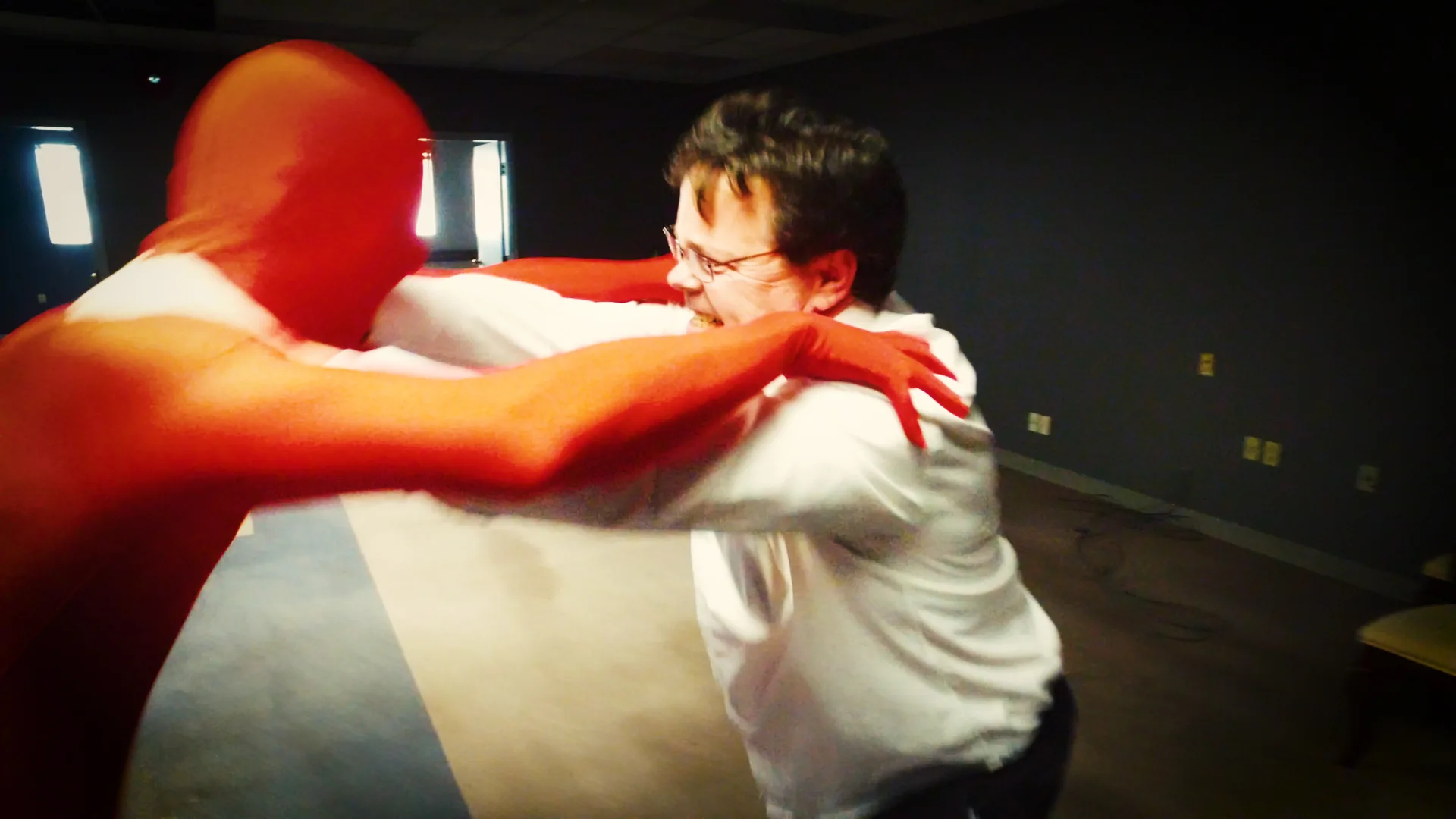 The mascot, alive. A frame from the edit — the performer in the full red suit locked in a comic grapple with a man in a white shirt. The show's central image.