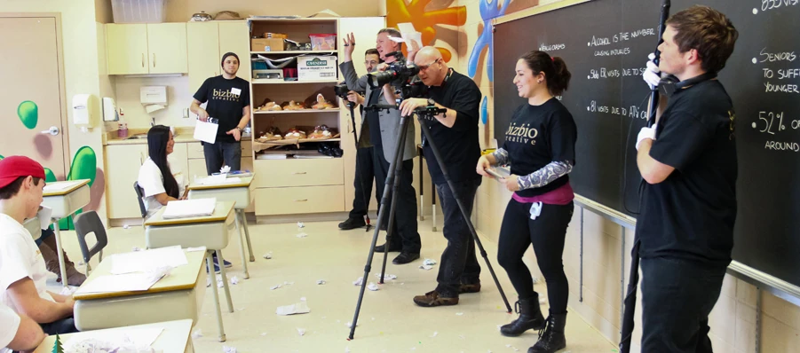 The idea. The crew filming the teenagers in matching shirts — the same class, older, one seat emptier.