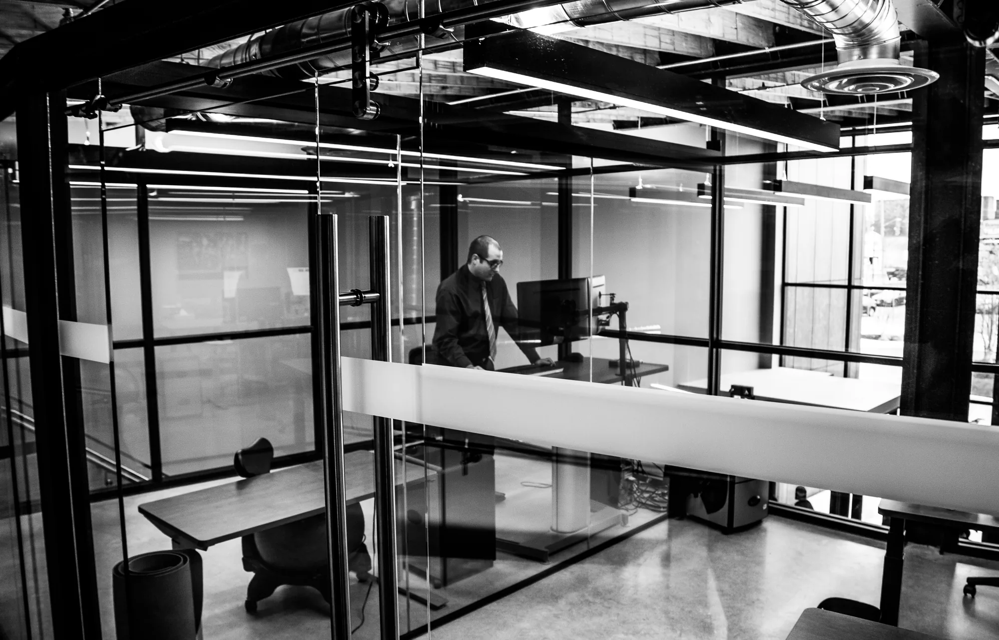 A man at his desk inside a glass-walled cubicle.