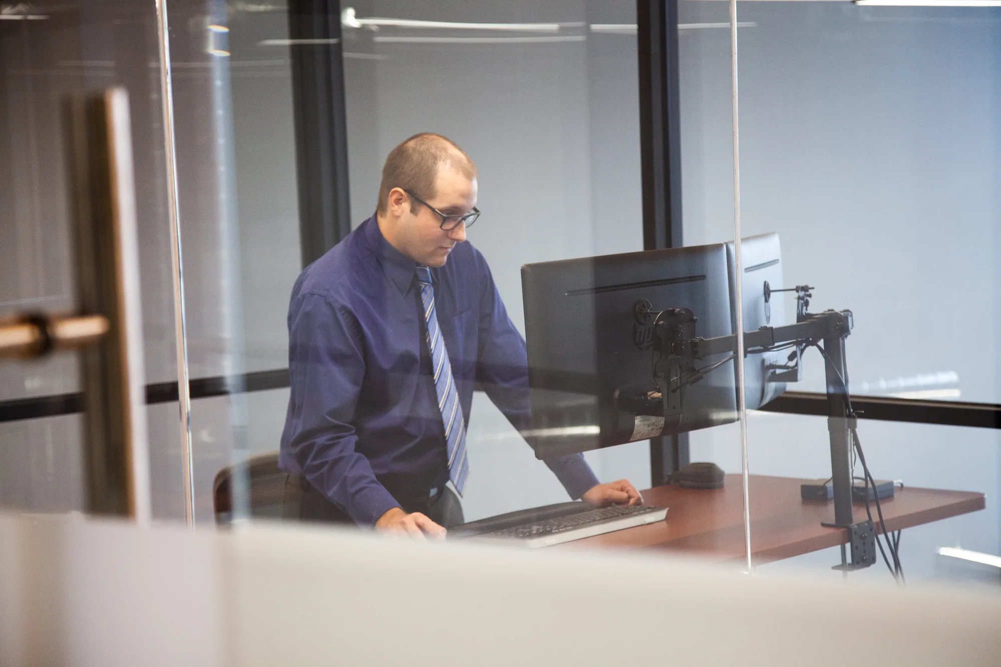 A man at a computer, dark blue shirt and striped tie.