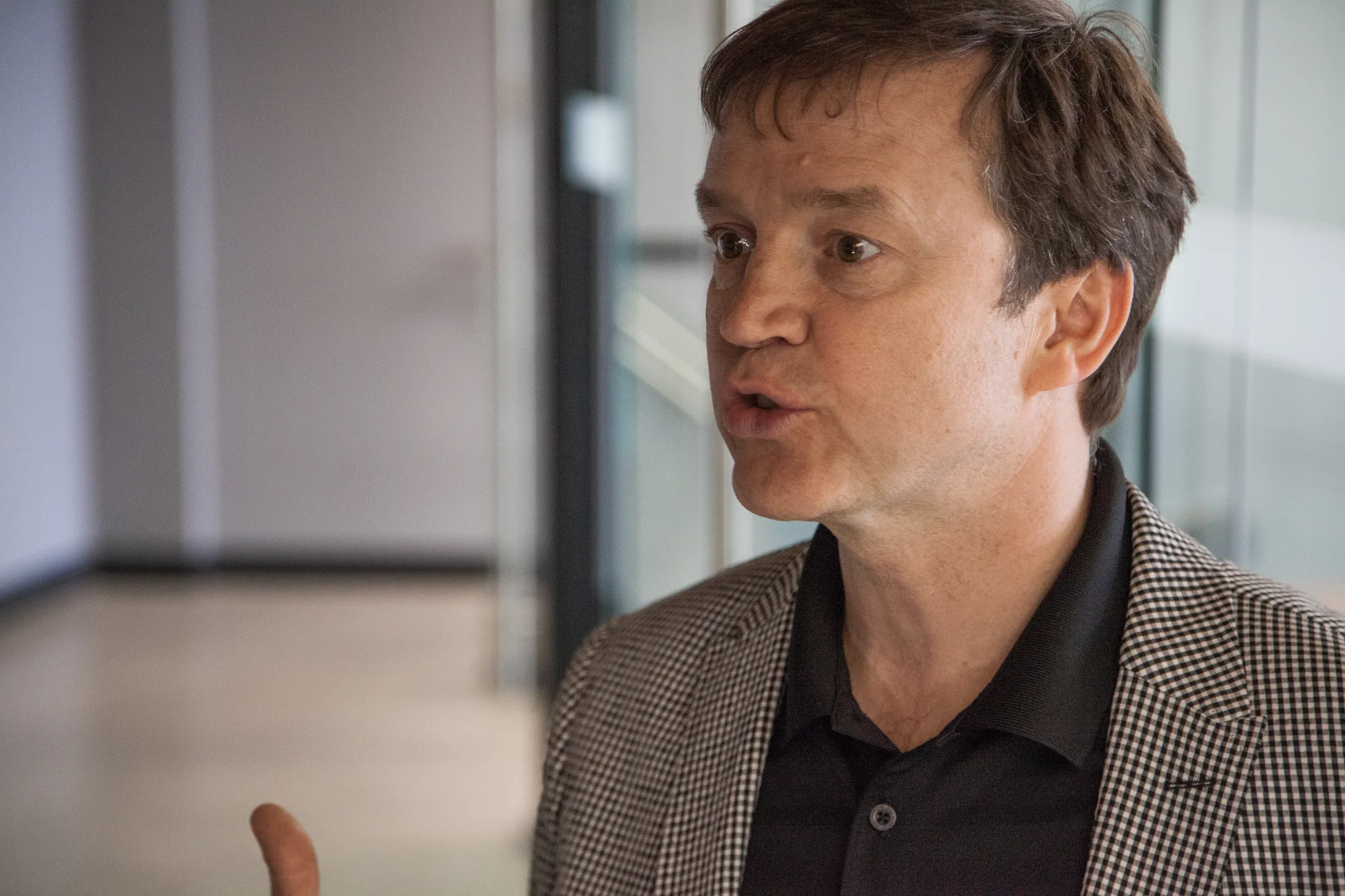 A man in a checkered blazer, mid-sentence, hand raised.
