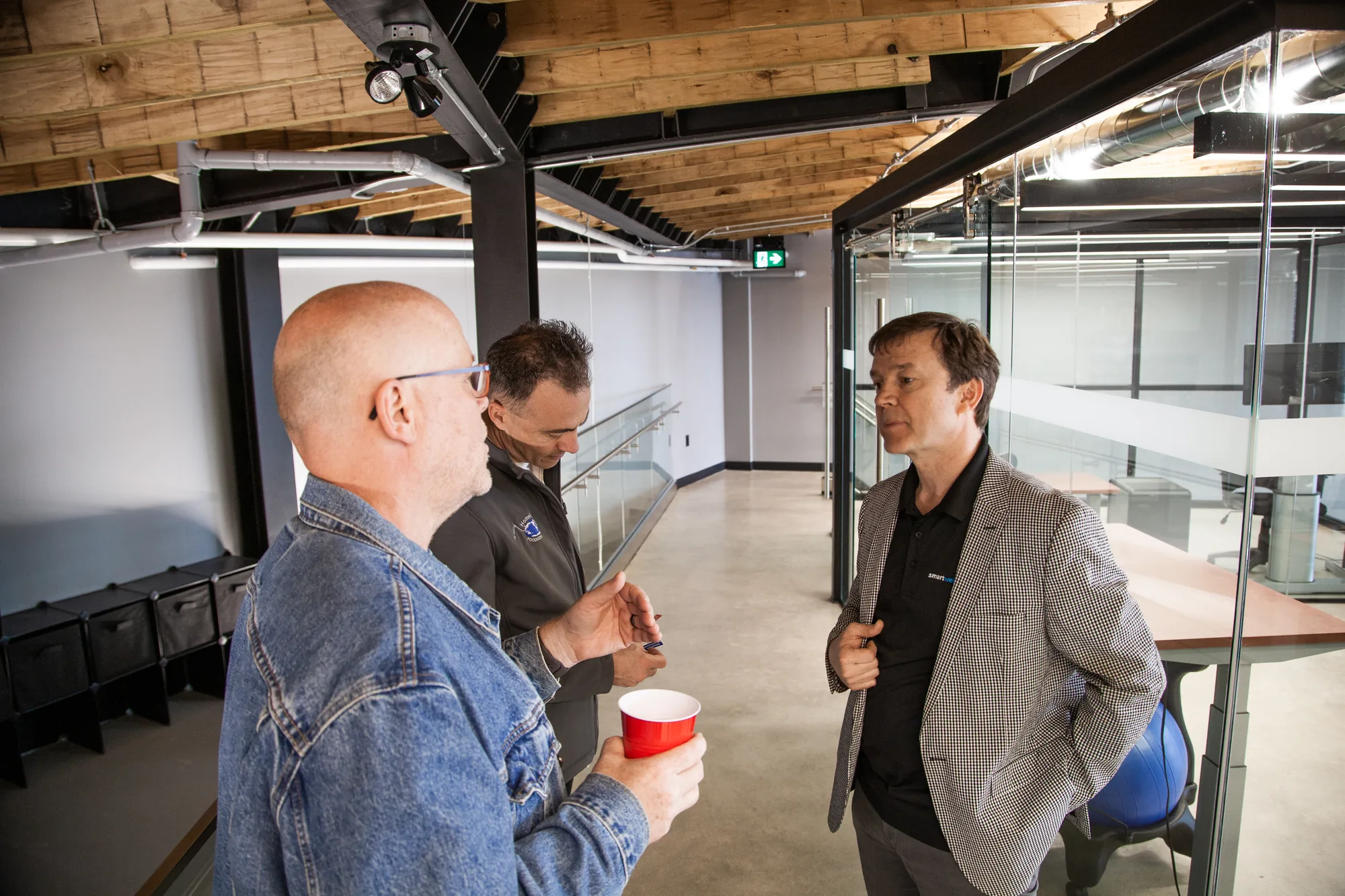 Three people in conversation; one is holding a red cup.